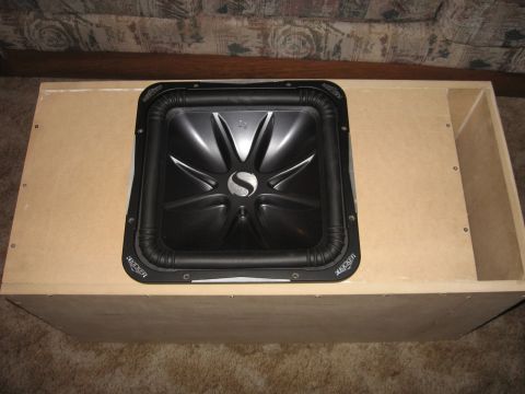 1992 Ford Crown Victoria - A square Kicker subwoofer is installed in a custom-built wooden enclosure, resting on a carpeted floor.