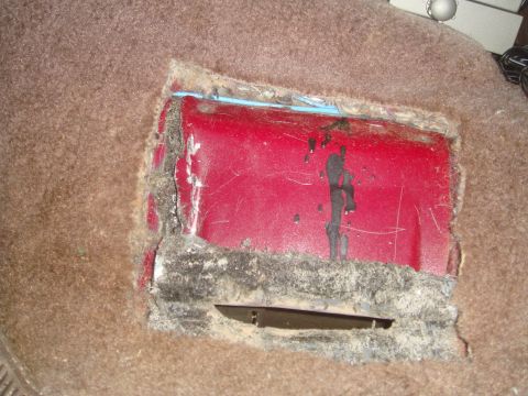 1992 Ford Bronco - This photo shows a red metal panel exposed by a cutout in the vehicle's carpeted floor.