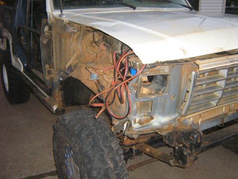 1986 Ford Bronco - The front end of a 1986 Ford Bronco shows significant damage and exposed wiring, with the grille and fender area visible.
