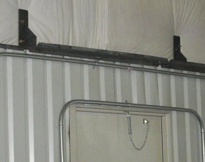Black steel rail on welded brackets mounted high on ribbed metal shop wall above a tan door