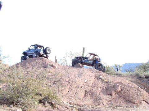 1987 Suzuki Samurai - Two off-road vehicles, including a 1987 Suzuki Samurai, navigate a desert landscape on a sunny day.