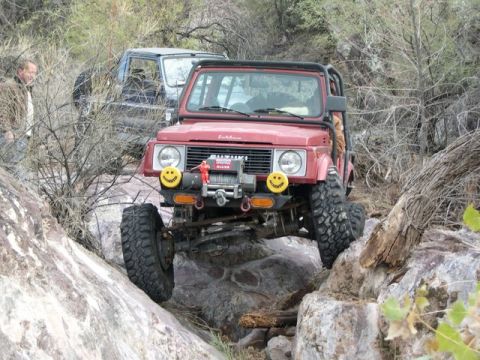 1987 Suzuki Samurai - A red 1987 Suzuki Samurai navigates a rocky trail, with another vehicle visible in the background.