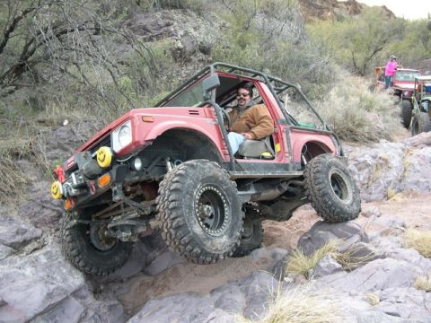 1987 Suzuki Samurai - A modified 1987 Suzuki Samurai navigates a challenging rocky terrain with other vehicles in the background.