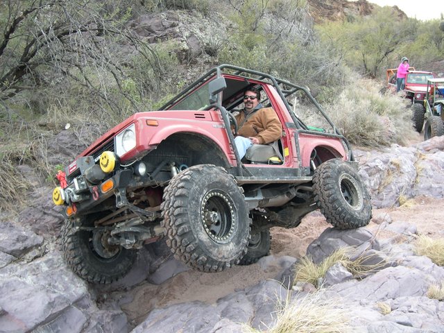 red 1987 Suzuki Samurai on rocky trail, driver in front, other vehicles behind