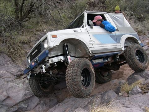 1987 Suzuki Samurai - A white 1987 Suzuki Samurai navigates a rocky trail with its tires angled on the uneven terrain.