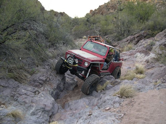 Red 1987 Suzuki Samurai navigating a rocky canyon, modified with off-road tires and roll cage