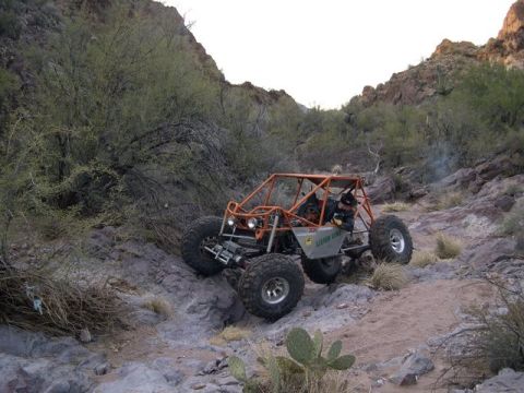 1987 Suzuki Samurai - Custom off-road buggy with orange roll cage navigates a rocky desert trail.
