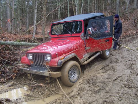 2002 Ford Sport Trac - This red Jeep is deep in the mud on a forest trail, with a person attempting to pull it out.