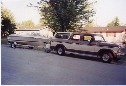 1979 Ford Bronco - A man works on the hitch of a trailer carrying a boat, which is being towed by a two-tone Ford Bronco.