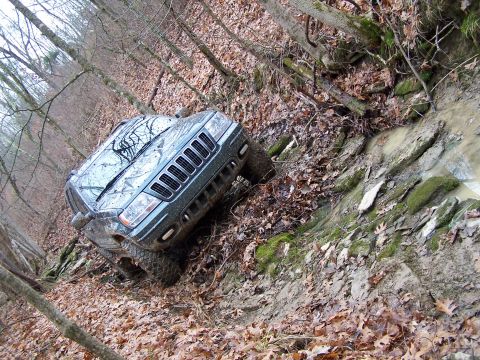 2002 Ford Sport Trac - A Jeep Grand Cherokee is shown off-roading on a wet, leaf-covered trail with a muddy ditch to its right.