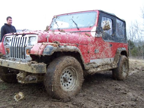 2002 Ford Sport Trac - A red Jeep Wrangler is stuck in the mud, with a person standing behind it.