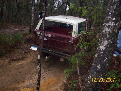 1978 Ford Bronco - 1978 Ford Bronco navigating a muddy off-road trail, showing its rear profile and white hardtop.