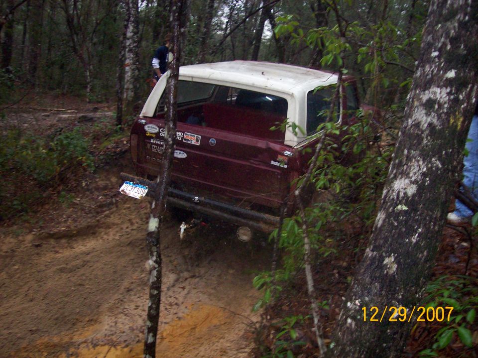 Maroon SUV with white top and decal-covered tailgate on a muddy wooded trail