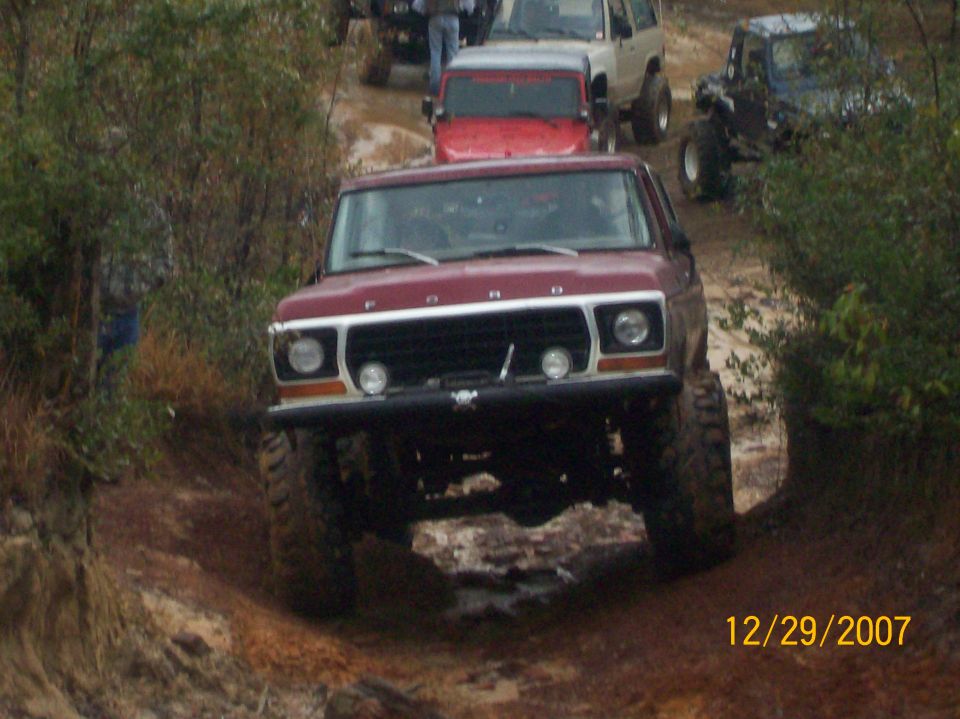Maroon 1970s Ford Bronco head-on on a muddy trail with a line of 4x4s waiting behind