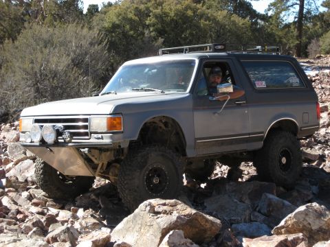 1996 Ford Bronco - Modified gray Ford Bronco driving over rocks off-road.