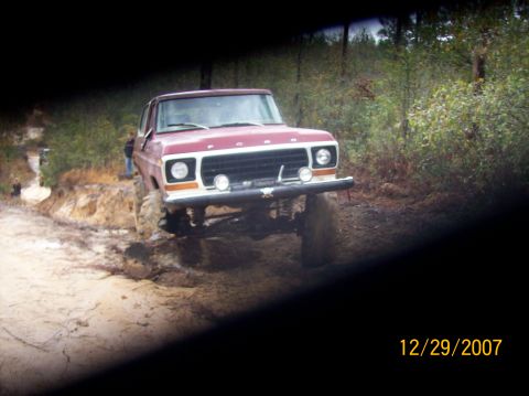 1978 Ford Bronco - This lifted Ford truck navigates a muddy trail with dense foliage in the background.