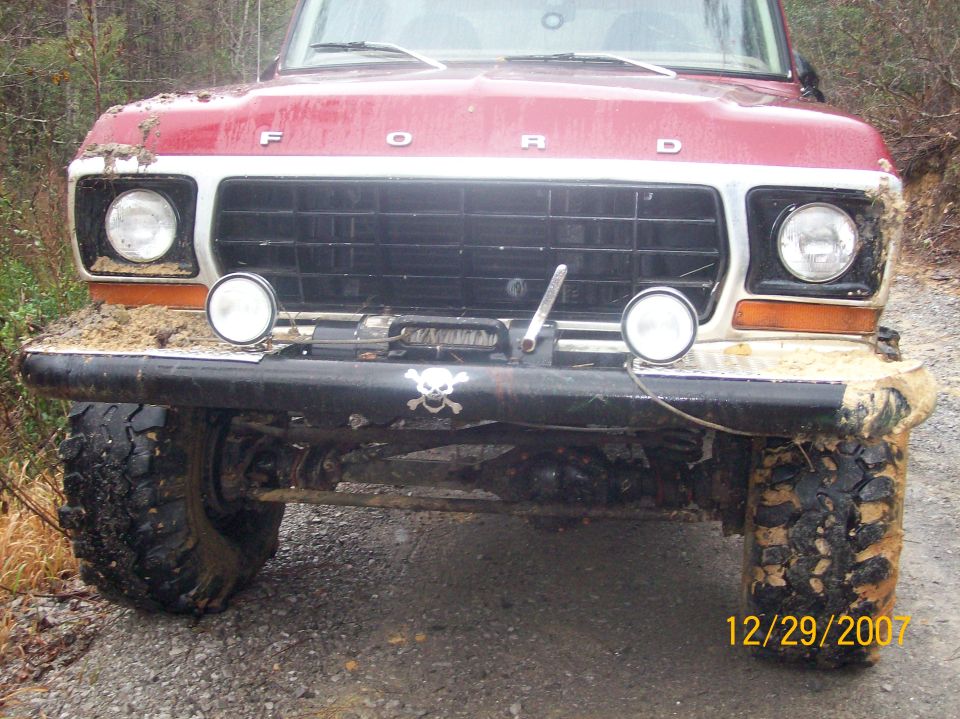 Red 1978 Ford Bronco front end covered in mud, with a skull and crossbones sticker on the bumper