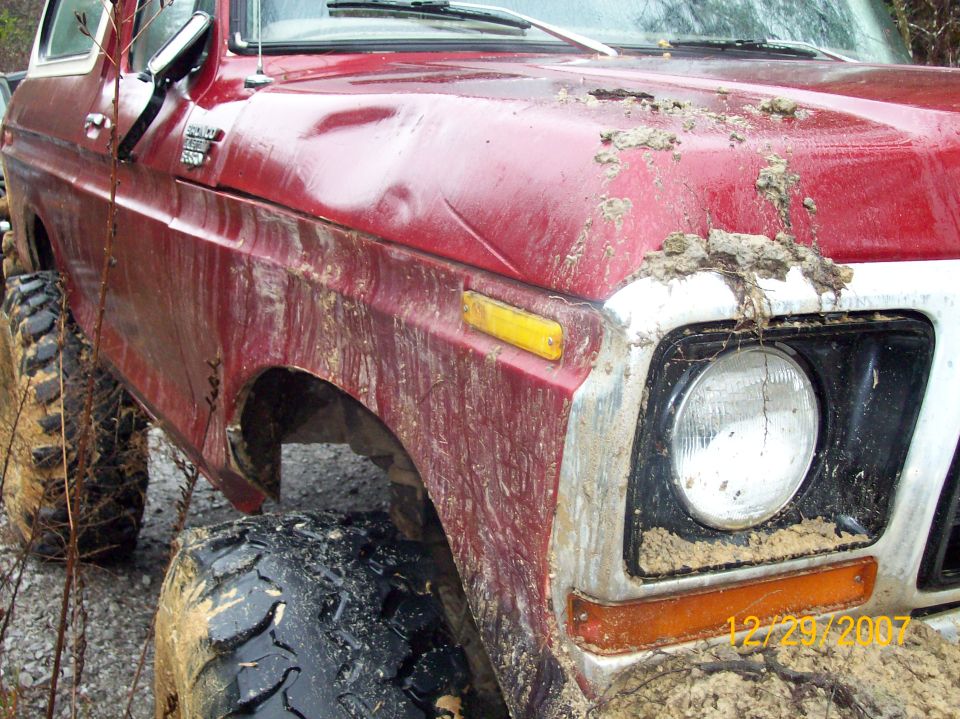 Red 1978 Ford Bronco with large tires, covered in mud
