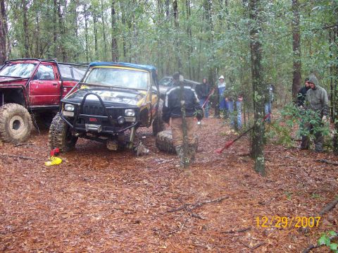 1978 Ford Bronco - Several off-road vehicles are parked in a wooded area with people gathered around.