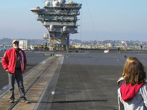 1989 Ford F-250 - Two people stand on the deck of an aircraft carrier, with the ship's island structure visible in the background under a clear sky.