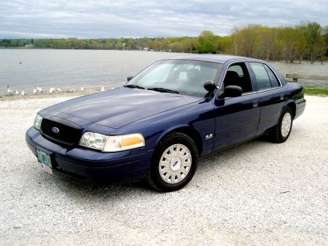 2003 Ford Crown Victoria - A dark blue 2003 Ford Crown Victoria is parked on a gravel lot next to a lake.