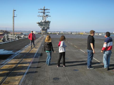 1989 Ford F-250 - Tourists gather on the flight deck of an aircraft carrier, with the ship's island structure towering in the background under a clear blue s…