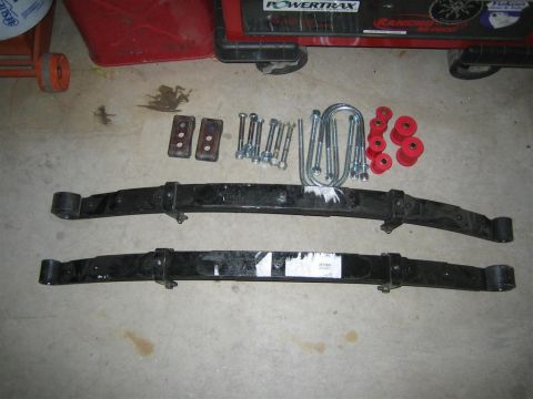 1987 Suzuki Samurai - Suspension parts laid out on a concrete floor, including leaf springs, U-bolts, and bushings.