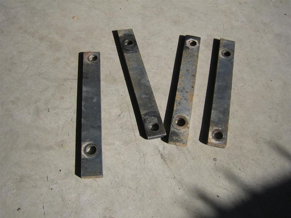 four metal brackets with holes on a concrete surface