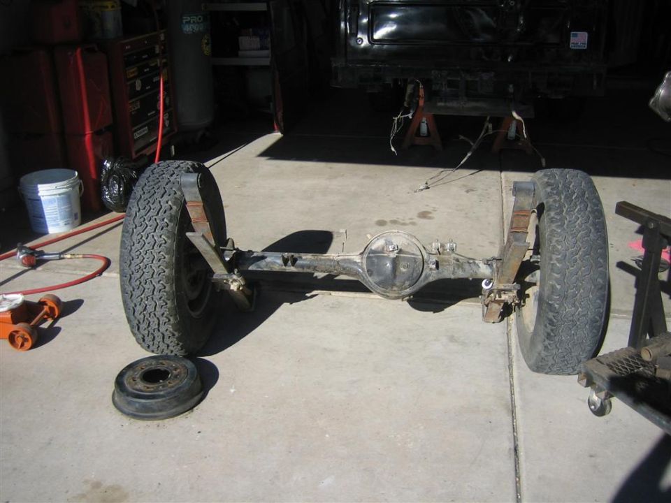 vehicle rear axle with two wheels and leaf springs, sitting on garage floor