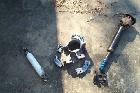 1996 Ford Bronco - Various automotive parts, including a driveshaft and differential components, lie on a concrete surface.