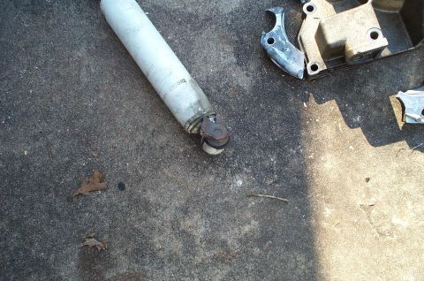 1996 Ford Bronco - A white-bodied shock absorber lying on a concrete driveway with its eyelet mount and rubber bushing visible, next to a rusty cast bracket a…