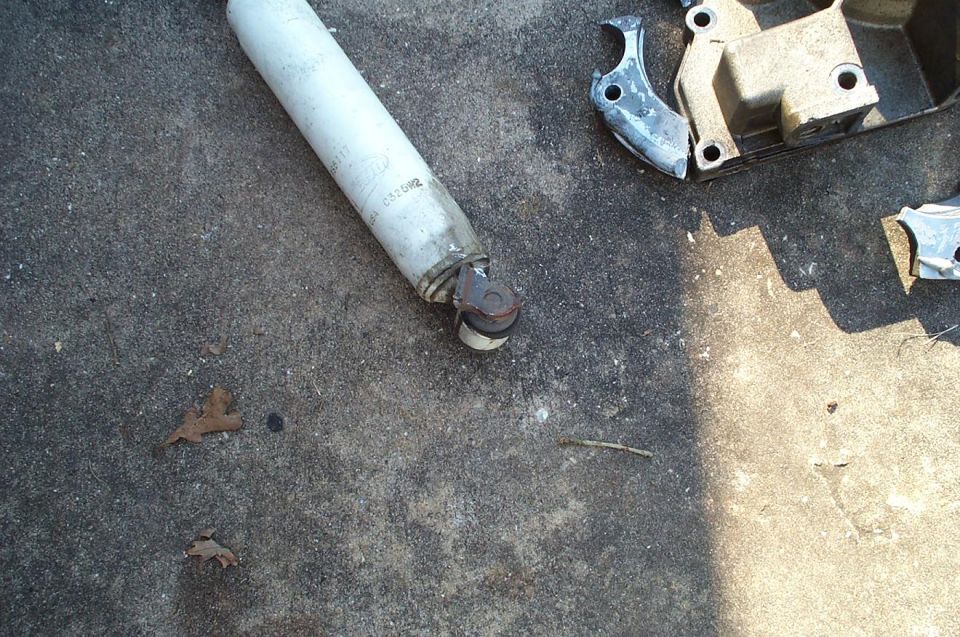 White shock absorber and rusty bracket laid out on a concrete driveway