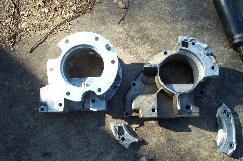 1996 Ford Bronco - Two cast aluminum transmission/transfer case adapter housings laid side by side on a concrete driveway, a clean replacement at left and a c…