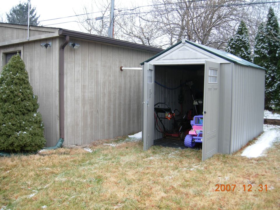 Gray storage shed with open door beside a garage in winter