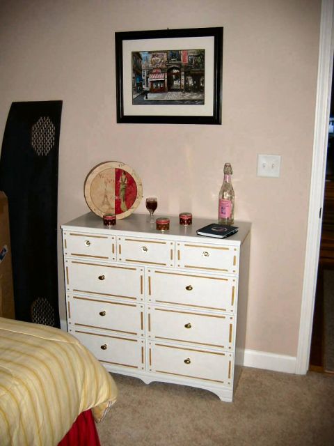 1985 Ford Crown Victoria LTD - A dresser is decorated with a framed picture, a decorative plate, and a bottle of pink champagne.