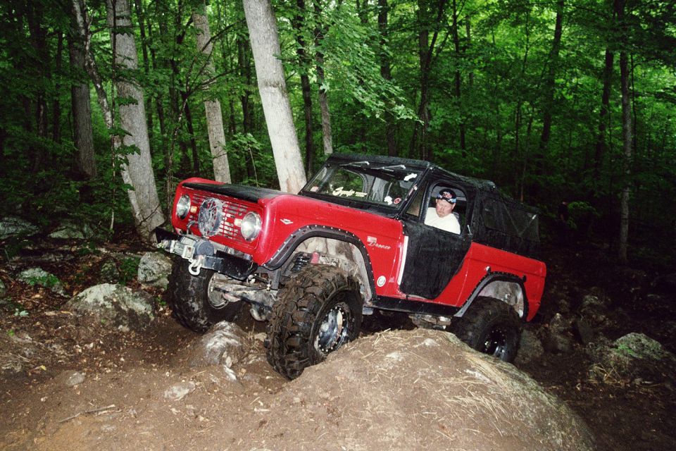 red SUV with black top going over rocks in woods