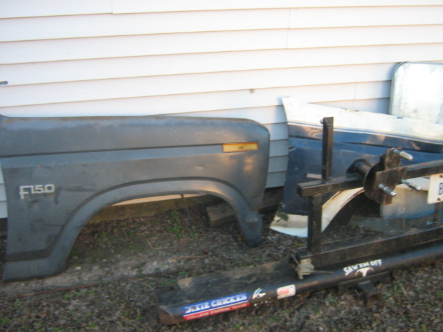 Gray Ford fender with F150 badge and blue body panel lying on ground by a house