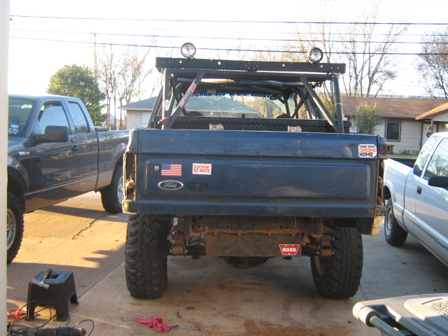 Rear of dark blue lifted Ford truck with roll cage, mud tires and stickers on tailgate