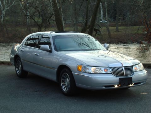 2002 Lincoln Town Car - A silver 2002 Lincoln Town Car is parked outdoors with a body of water and trees in the background.