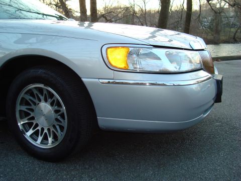 2002 Lincoln Town Car - A close-up view of the front passenger side of a silver Lincoln Town Car, parked outdoors near trees and water.