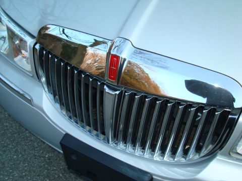 2002 Lincoln Town Car - Close-up of a silver Lincoln Town Car's chrome grille, showing vertical bars and the red Lincoln emblem.