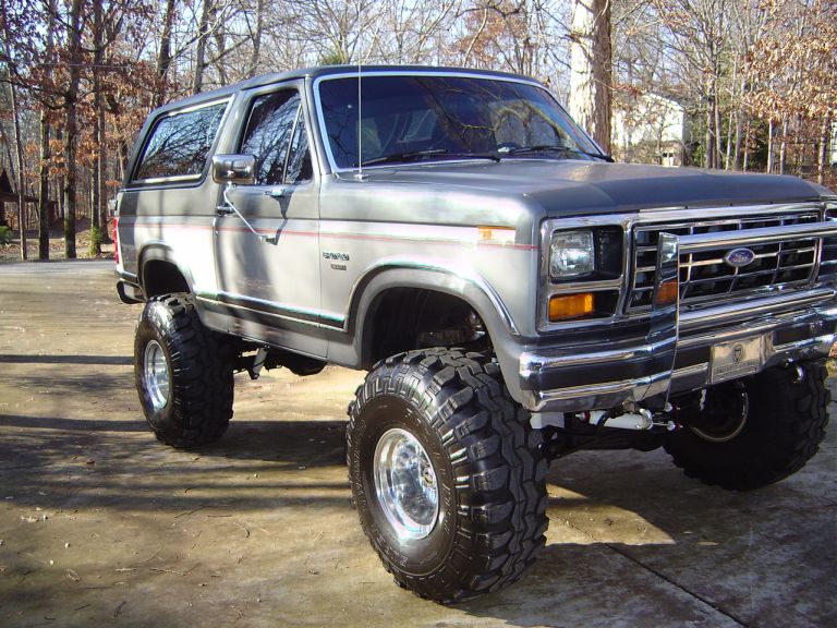 Silver lifted Ford Bronco with large off-road tires, chrome grille, and aftermarket bumper