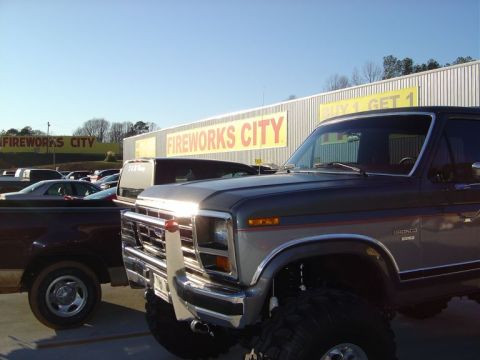 1986 Ford Bronco - A two-tone gray Ford Bronco is parked in front of a Fireworks City store.