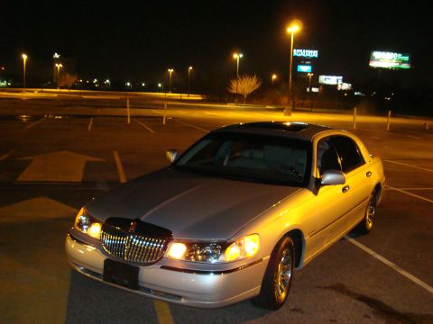 2002 Lincoln Town Car - A silver 2002 Lincoln Town Car is parked in an empty lot at night, its headlights on.