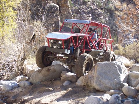 1981 Ford F-150 - A custom-built red buggy with large tires maneuvers over a rocky trail in a desert canyon.