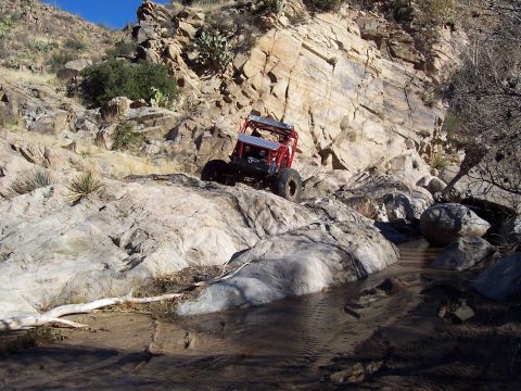 1981 Ford F-150 - A custom off-road buggy navigates a challenging rocky terrain with a small stream at the bottom.