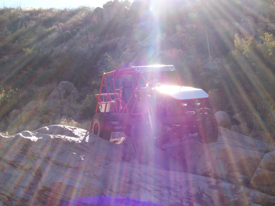 Buggy with red roll cage driving over rocks in a sunny, arid landscape