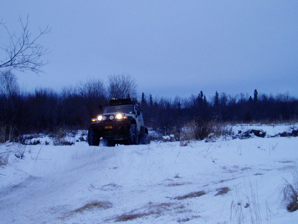 Jeep Wrangler with roof rack driving on a snowy hill, trees in background