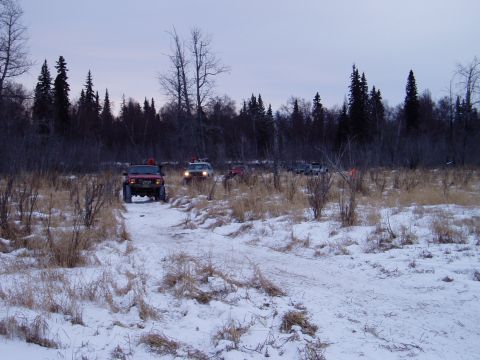 2000 Ford E350 - Several off-road vehicles navigate a snow-covered trail surrounded by trees and dry vegetation.