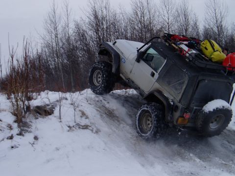 2000 Ford E350 - Jeep Wrangler Rubicon navigates a challenging snowy terrain with its cargo rack fully loaded.